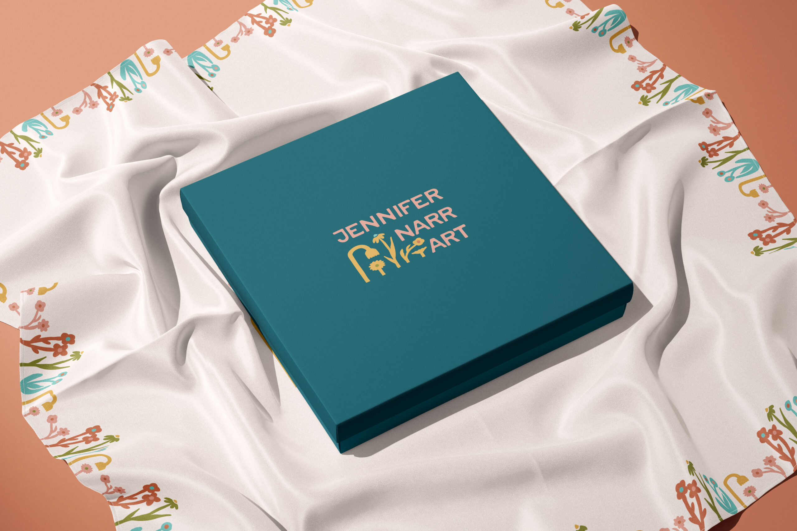 A box with an embossed artist logo on top of a floral scarf.