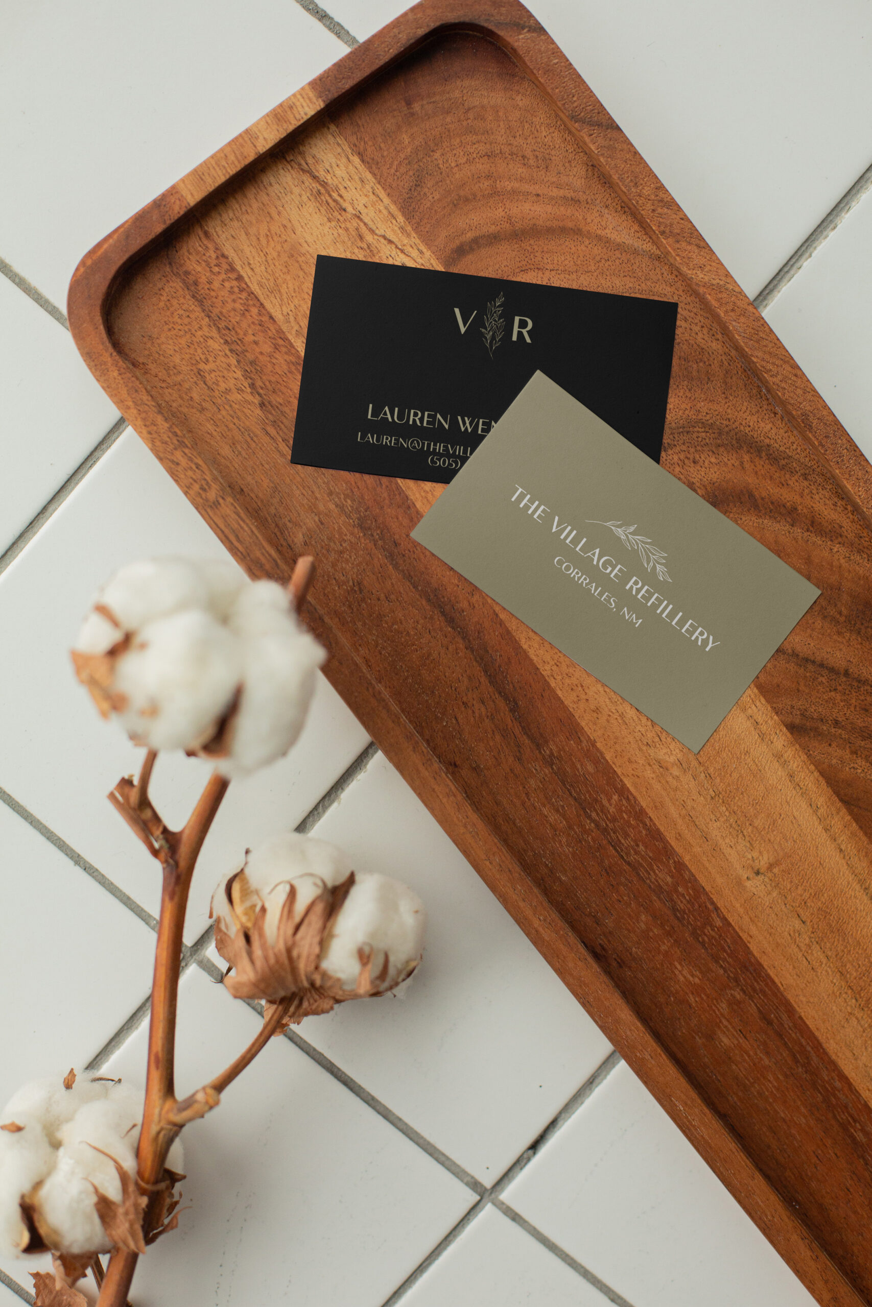 Business card with the Village Refillery logo resting on a wooden plate.